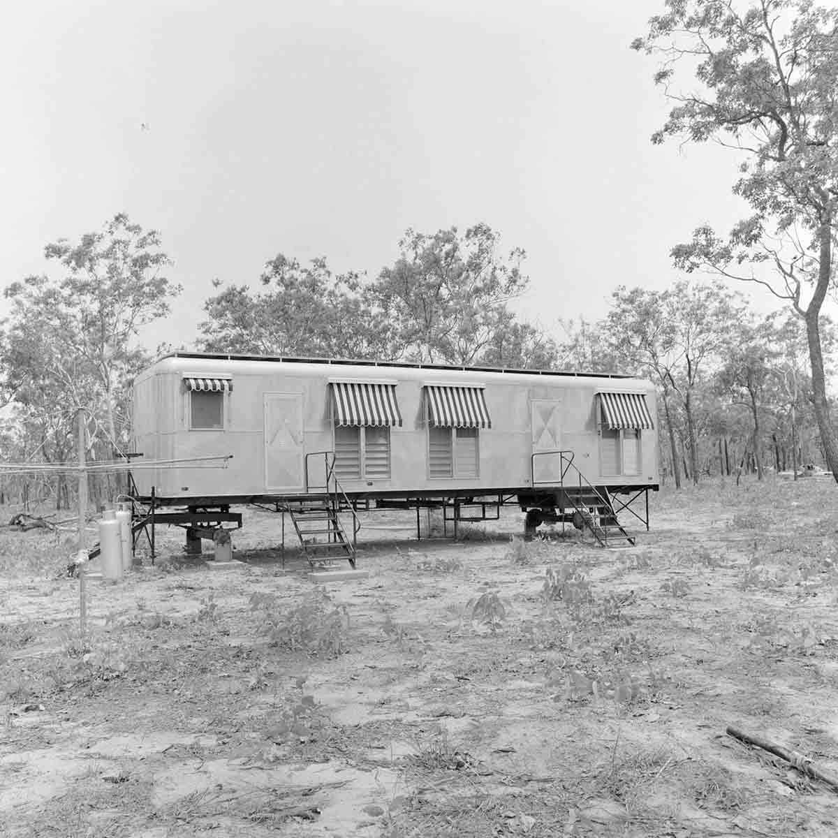 Semi-elevated metal (?) house with louvre windows and canvas awnings with bushland behind