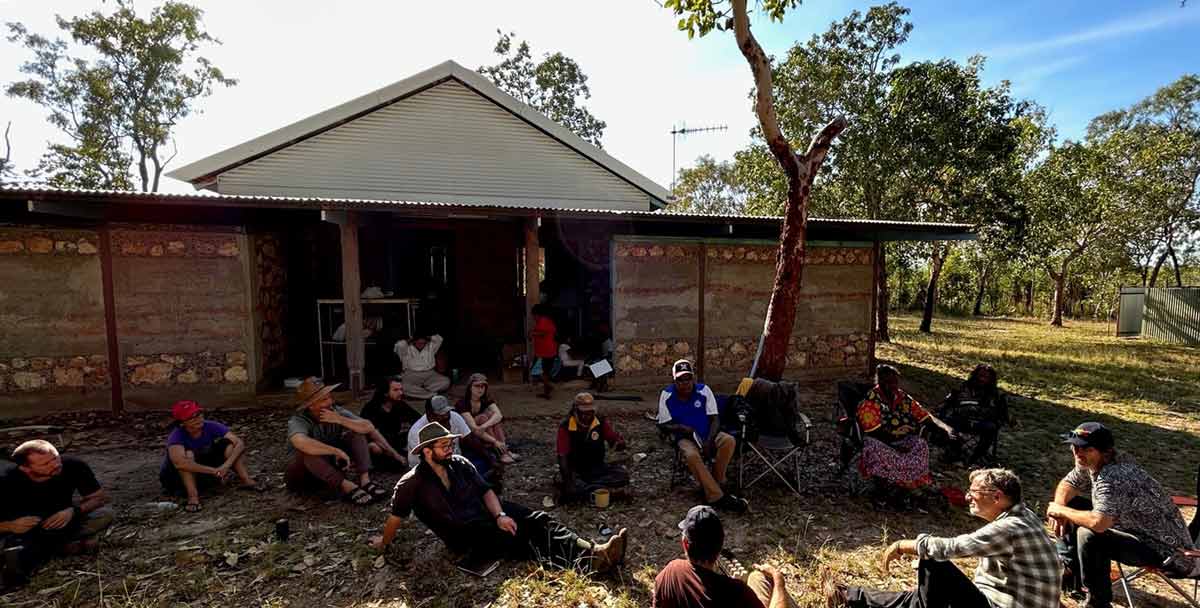Warumungu people, a Rembarrnga man and architects and engineers sit outside a community-built house at Barapunta homeland.  